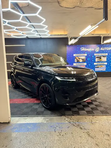 Musta Range Rover Sport pesuhallissa Hämpin Autopesun banneri taustalla